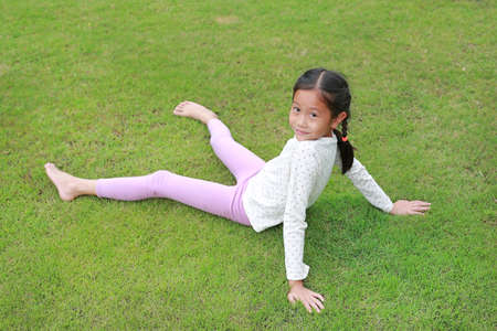 Smiling Asian young girl child lying on green lawn at the garden. Kid lies on grass with looking camera.の写真素材