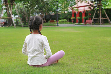 Back view Asian young girl kid practicing mindfulness meditation sitting on lawn in the garden. Peaceful concept.の写真素材
