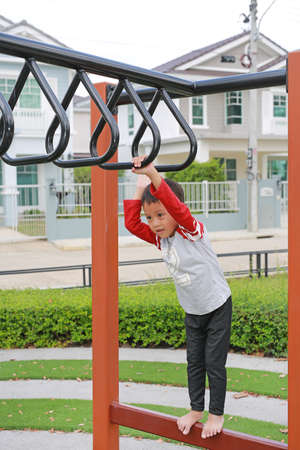 Asian little boy having fun playing on equipment at a playground.