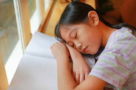 Portrait of Asian young girl child sleeping on a book near the windows. Education and resting concept.の写真素材