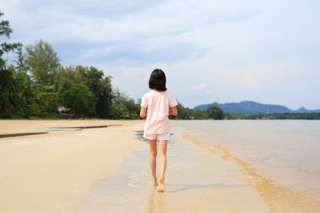 Back view of Asian girl child walking alone on tropical sand beach.の写真素材