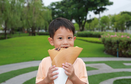 Little boy eating crispy crepe dessert in the garden.の写真素材