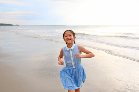 Portrait of Asian young girl kid running on tropical sand beach at morning sunrise.の写真素材