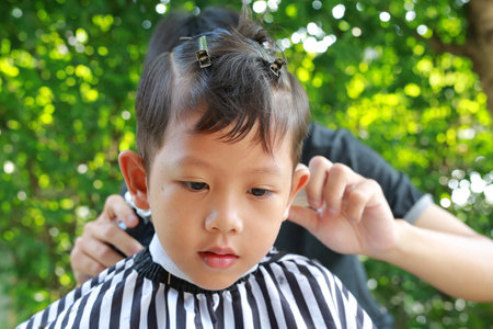 Asian boy cut in hairdresser's machine in the gardenの写真素材