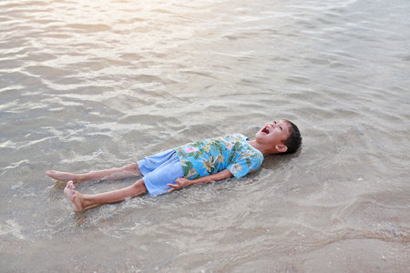 Happy Asian little boy laughing and enjoy lying on tropical beach at sunrise. Adorable little child kid having fun in summer holiday.の写真素材