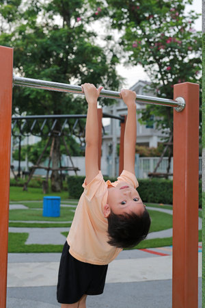 Asian little boy having fun hanging on playing equipment at a playground.の写真素材