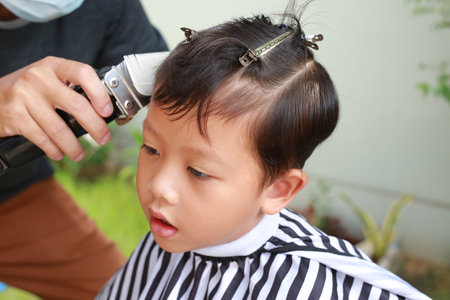 Asian boy cut in hairdresser's machine in the gardenの写真素材