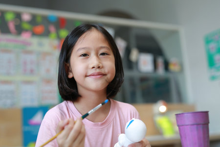 Asian young girl painting a doll with watercolor. Kid with water color painting activity.の写真素材