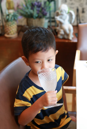 Portrait of Asian little boy drinking water from glass while sitting at restaurant.の写真素材