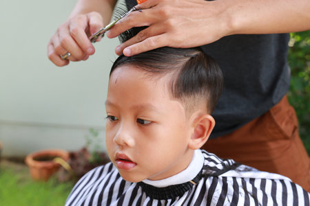 Cutting hair of Asian little boy with barber scissors in the garden.の写真素材