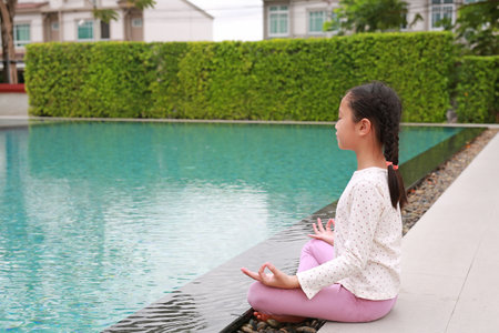 Peaceful Asian young girl kid practicing mindfulness meditation sitting near the pool.の写真素材