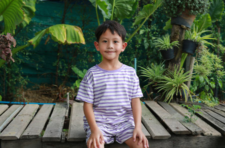 Portrait of Asian little boy sitting on small wood bridge in the garden.の写真素材
