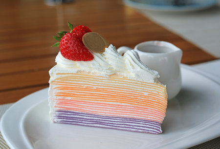 Layer cake slice topped with fresh strawberries and chocolate coin on white plate.の写真素材