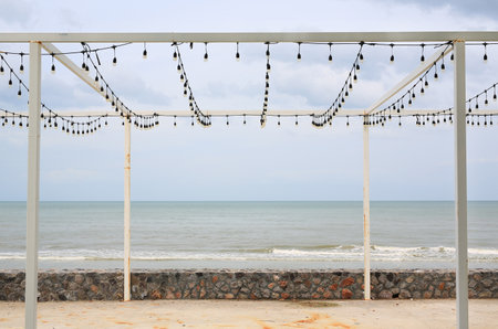Metal frame and luminous garland of bulbs at coast next to the sea.の写真素材
