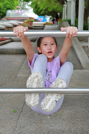 Portrait of Asian girl child enjoy to climbing aluminum fence in public park.
