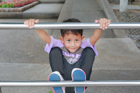 Asian little boy kid having fun to climbing aluminum fence in public park.