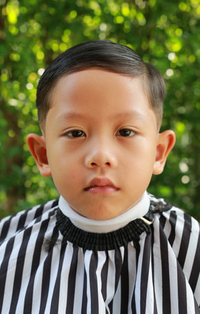 Cutting hair of Asian little boy with barber scissors in the garden.の写真素材