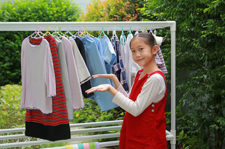Asian girl child helping to do dry the clothes at the garden near house. Kid hanging cloth on a clothesline.の写真素材