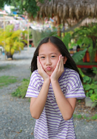 Portrait of happy Asian girl child touching her chin with funny mouth while stay in garden.の写真素材