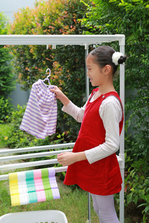 Portrait of happy Asian girl hanging the laundry on a clothes rail with looking camera at garden near house.の写真素材