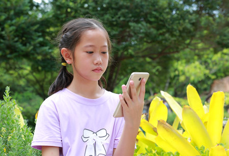 Portrait of Asian girl child looking smartphone screen while in park outdoor. Distant communication concept.の写真素材