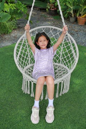 Smiling Asian girl child while sitting and relaxing on the white cradle or swing in the garden.の写真素材