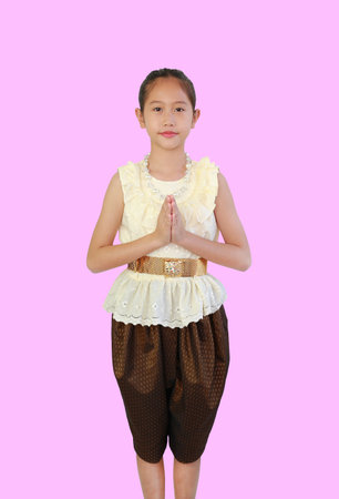 Tidy Asian girl child in traditional Thai dress with Pay respect, Sawasdee symbol, Welcome expression on pink background, front view and clipping path.の写真素材