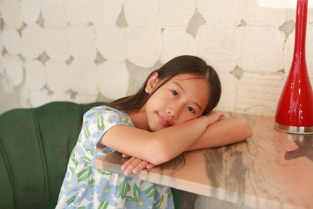 Smiling Asian girl child age about 9 years old sit on sofa chair and lying on marble table with looking camera.の写真素材