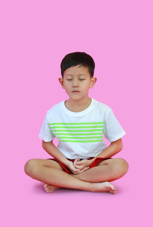 Asian boy kid practicing mindfulness meditation sitting isolated on pink background, Peaceful concept.の写真素材