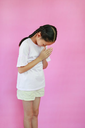 Pretty Asian young girl ages 9 years old Pay respect or pray posture isolated on pink studio background. Side view.の写真素材