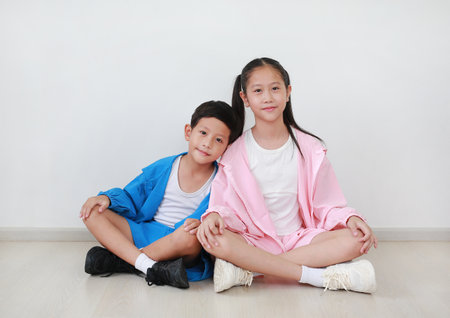 Portrait of Asian boy kid and girl child leaning against each other while sitting in white room and looking camera.の写真素材