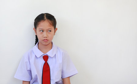 Unhappy with bored face of Asian schoolgirl in school uniform looking beside on white background.