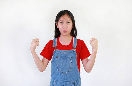 Surprised face expression and excited Asian girl child with fists up and raise arms on white studio background.の写真素材