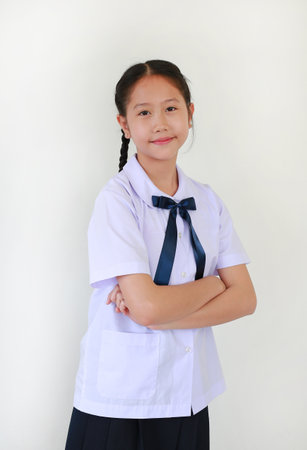 Portrait of smiling pretty Asian student girl in school uniform stand with arms crossed against white studio background.の写真素材