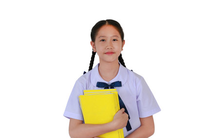 Pretty Asian student girl in school uniform cuddle a yellow book while standing isolated on white studio background. Schoolgirl back to school concept.の写真素材