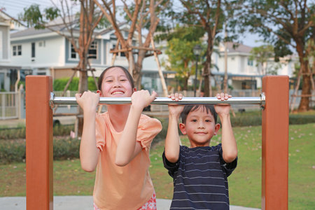 Portrait of Asian boy and girl child hanging on equipment at a playground.