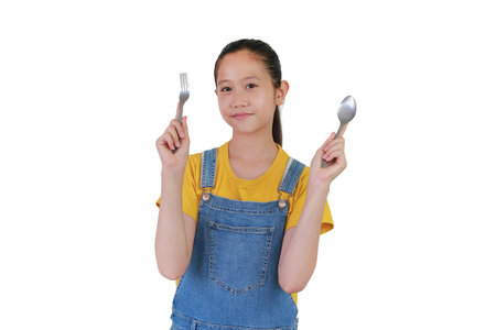 Happy Asian girl kid holding fork and spoon isolated  white studio background. Ready for a meal.の写真素材