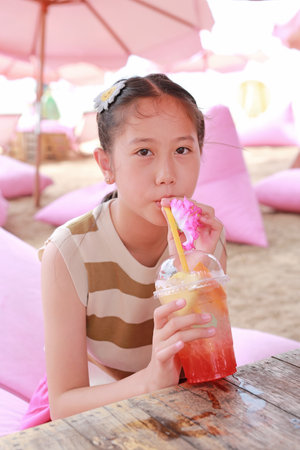 Portrait of Asian girl child drinking fruit juice while lying on the beach.の写真素材