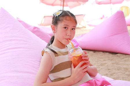 Pretty Asian young girl drinking fruit juice while lying on sofa bed near the beach.の写真素材