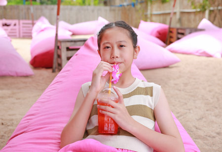 Portrait of Asian girl child drinking fruit juice while lying on sofa bed near the beach.の写真素材