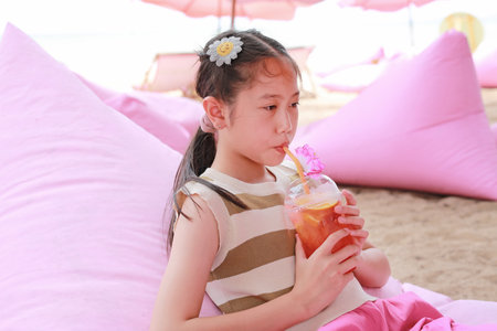 Portrait of Asian girl child drinking fruit juice while lying on sofa bed near the beach.の写真素材