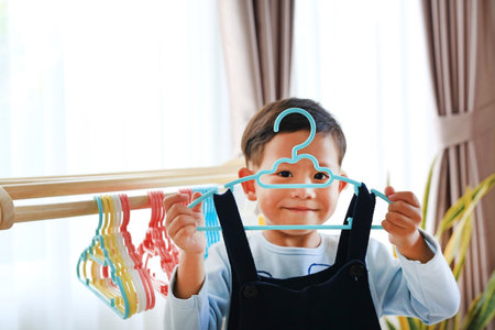 Asian little boy use hanger hang up a clothes on wood rack.の写真素材