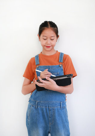 Portrait of Asian girl using a tablet and a stylus while draw, write, or work on a creative or educational project against white background.の写真素材