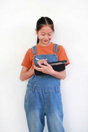 Portrait of Asian girl using a tablet and a stylus while drawing, writing, or working on a creative or educational project against white background.の写真素材