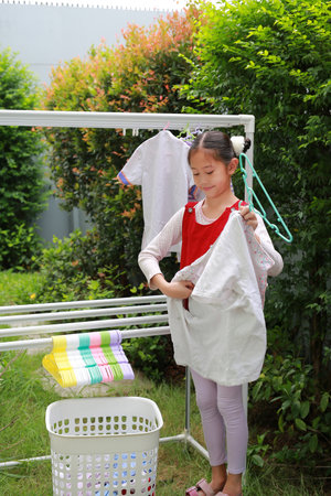 Asian girl child helping to do dry the clothes at the garden near house. Kid hanging cloth on a clothesline.の写真素材