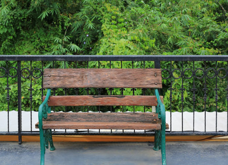An empty wooden bench sitting peacefully on a balcony, overlooking a lush curtain of green foliage,...