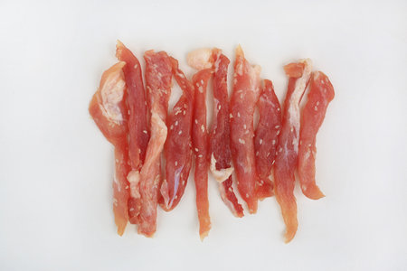 Marinated and sliced pork strips, seasoned with sesame seeds ready for sun-drying or grilling, presented on bright white background for food photography.の写真素材