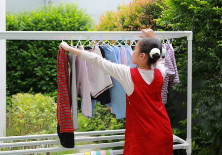 Portrait of happy Asian girl hanging the laundry on a clothes rail with looking camera at garden near house.の写真素材