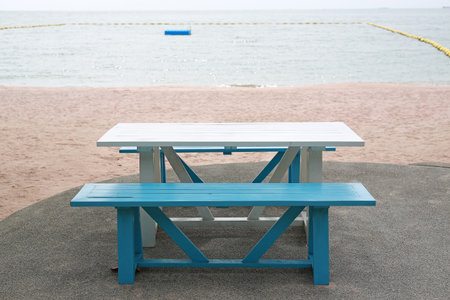 Serene coastal spot featuring a white wooden picnic table and blue benches, perfectly inviting...