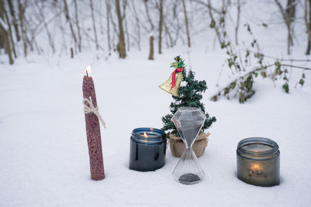Christmas toys, wax candle and senko on snow, burning candles, sprig of dried flowers in winter forestの写真素材
